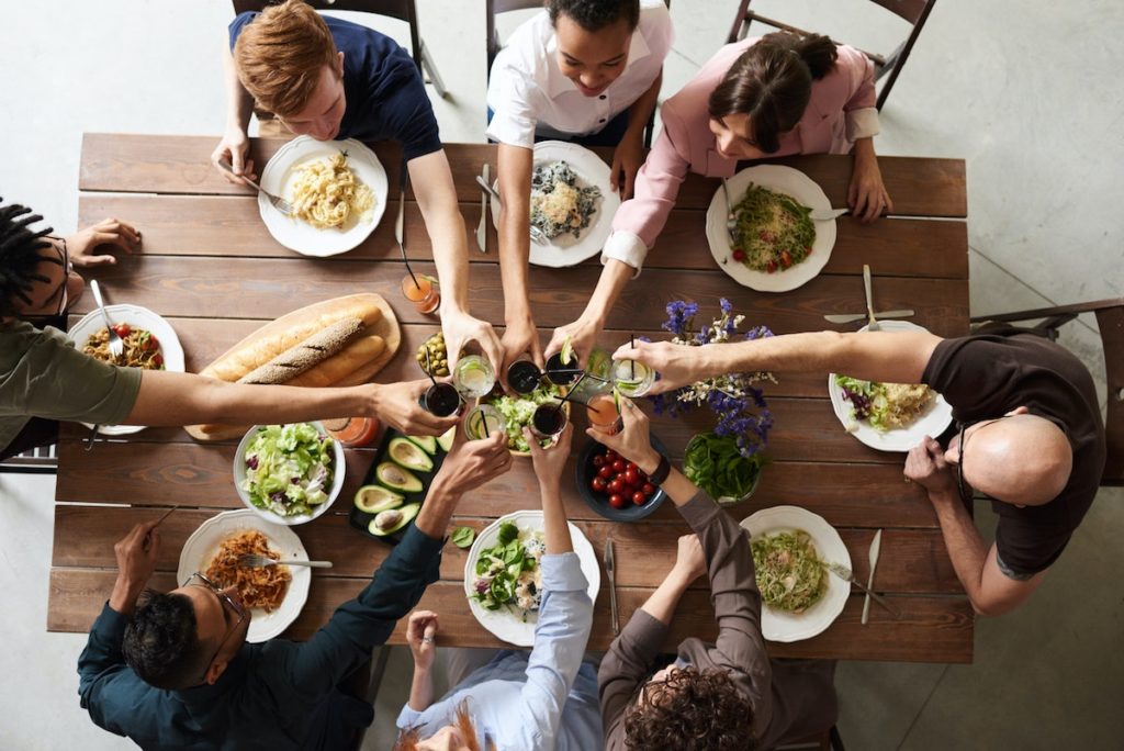 Friends surrounding and reaching in over a table full of food